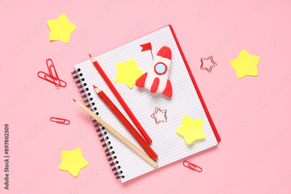 Rocket made of plasticine with notebook and pencils on pink background. Top view