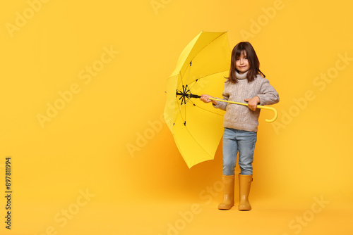 Cute little girl with bright umbrella on yellow background. Space for text