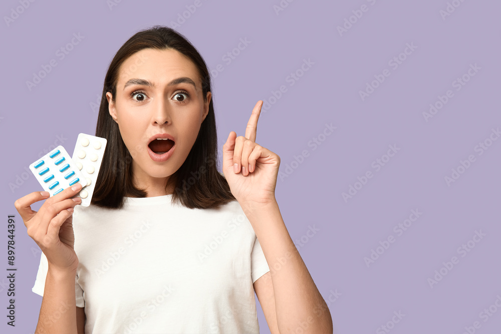 Shocked young woman with pills pointing up on lilac background Shocked young woman with pills pointing up on lilac background