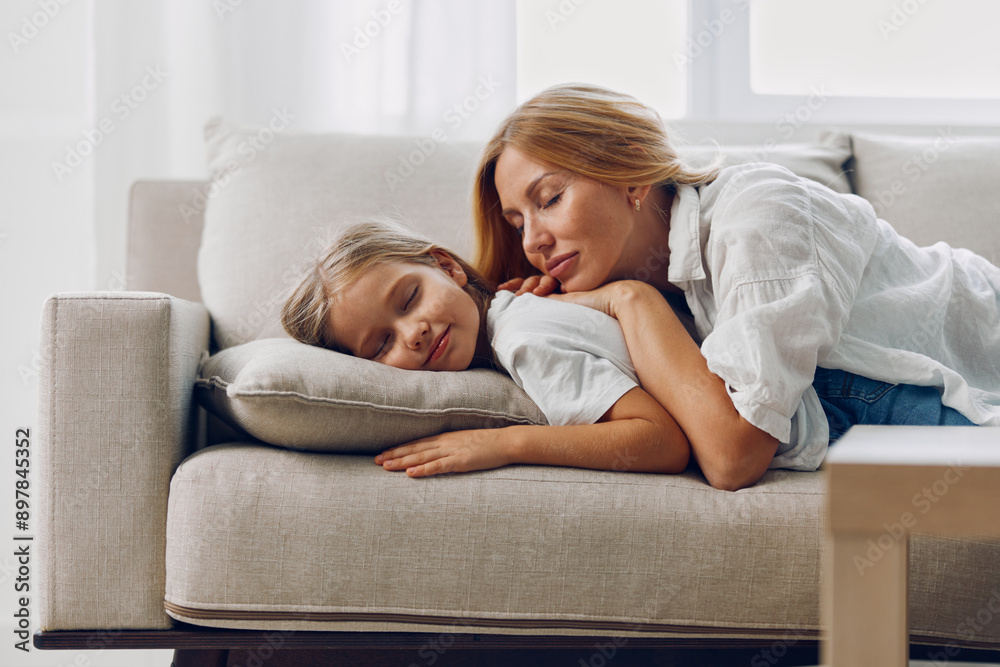 Mother and daughter relaxing on a couch in cozy living room with white wall background Mother and daughter relaxing on a couch in cozy living room with white wall background