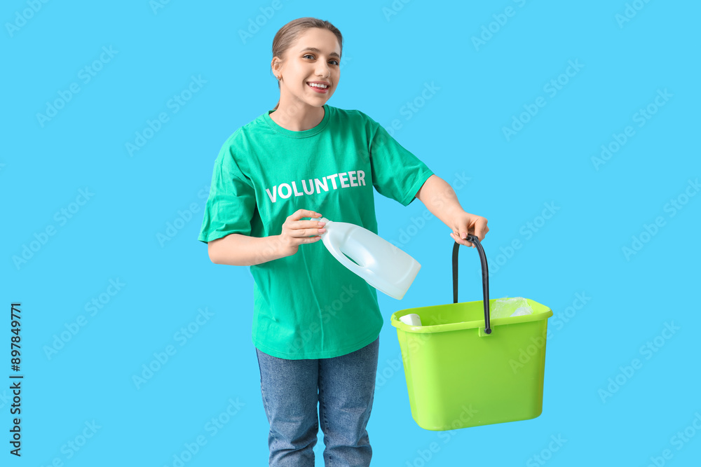 Female volunteer throwing plastic bottle into bin on blue background. Waste sorting concept Female volunteer throwing plastic bottle into bin on blue background. Waste sorting concept