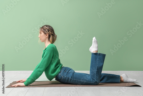 Young woman practicing yoga on mat near green wall photo