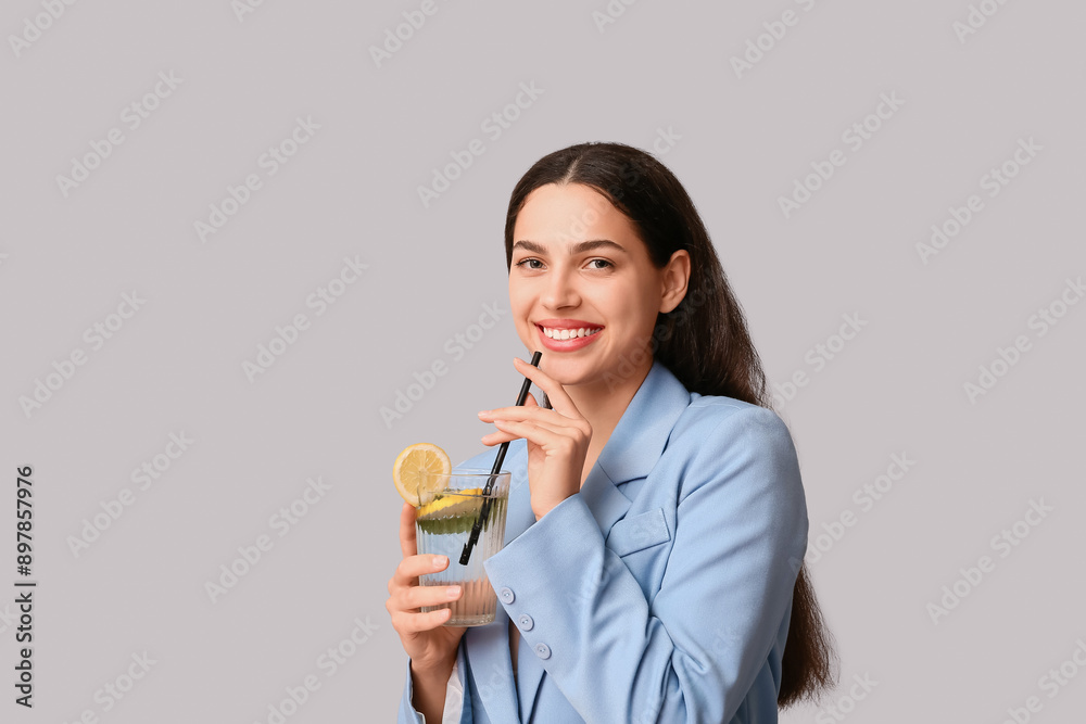 Beautiful young happy woman with glass of fresh lemonade on grey background Beautiful young happy woman with glass of fresh lemonade on grey background