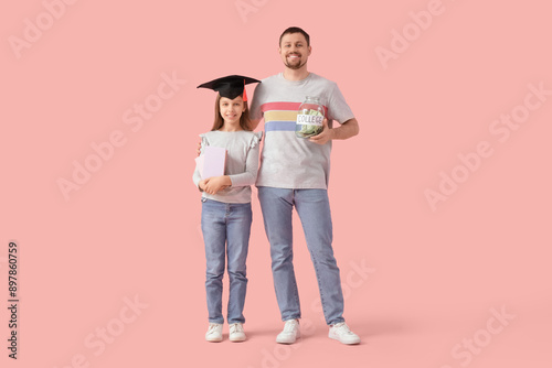 Father and his daughter in mortar board with books and money jar on pink background. Tuition fees concept