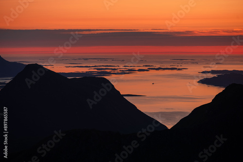 Silhouette of coastal northern Norwegian moutains against the setting and rising midnight sun at dusk and dawn. Dramatic colours and contrast, sun over arctic ocean and mountain ridges photo