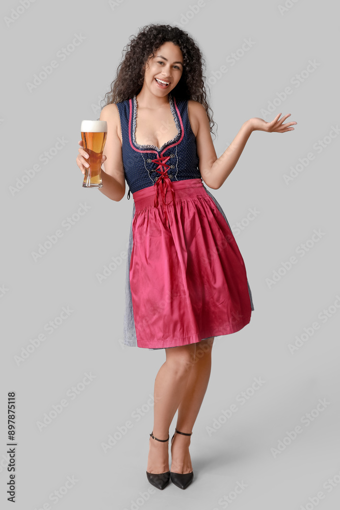Happy African-American woman with beer showing something on grey background. Octoberfest celebration Happy African-American woman with beer showing something on grey background. Octoberfest celebration