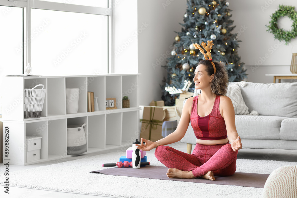 Sporty mature woman in reindeer horns meditating at home on Christmas eve Sporty mature woman in reindeer horns meditating at home on Christmas eve