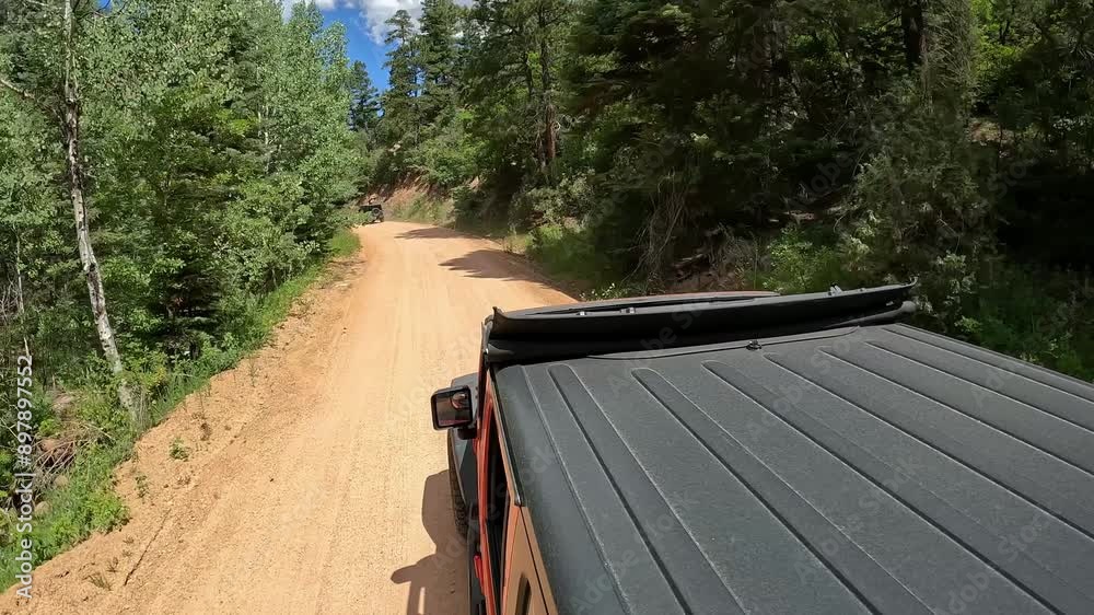 POV - View of vehicle rooftop while driving on a scenic byway in Rocky Mountains; graveled road with curves, granite embankments and trees; concepts of adventure and historic scenic byways POV - View of vehicle rooftop while driving on a scenic byway in Rocky Mountains; graveled road with curves, granite embankments and trees; concepts of adventure and historic scenic byways