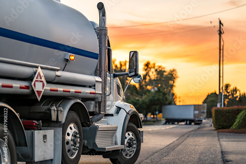 Industrial standard day cab big rig white semi truck transporting flammable liquids in tank semi trailer running on the local road at evening sunset time