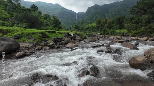 Stream flowing over small rocks with Shayadri hill in background, lush greenery during monsoon. photo