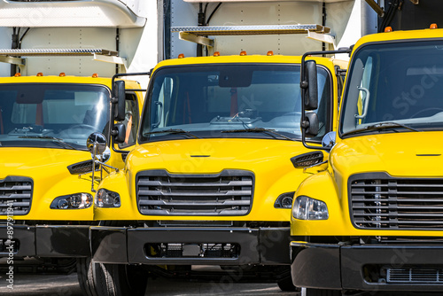 Yellow middle duty day cab rigs semi trucks with refrigerated box trailers standing in row on industrial parking lot