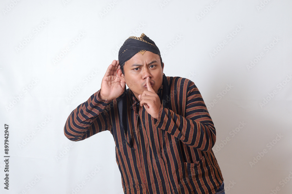 Portrait of serious Asian man in javanese cloth with blangkon hat whispering malicious talk conversation, hand on mouth telling secret rumor. Isolated image on white background Portrait of serious Asian man in javanese cloth with blangkon hat whispering malicious talk conversation, hand on mouth telling secret rumor. Isolated image on white background