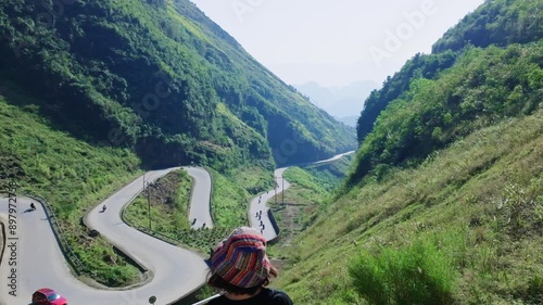 This footage captures the breathtaking landscape of Ha Giang in North Vietnam, featuring a girl gazing at a winding road nestled among lush green mountains. 
