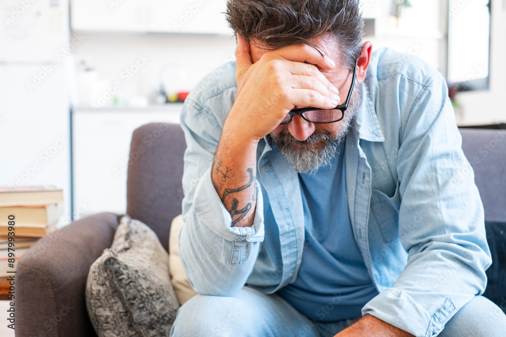 One man sitting on sofa alone at home touching forehead thinking at problems and ideas solution to solve. Financial crisis relationship breakup, divorce mature male worried and stressed in living room One man sitting on sofa alone at home touching forehead thinking at problems and ideas solution to solve. Financial crisis relationship breakup, divorce mature male worried and stressed in living room