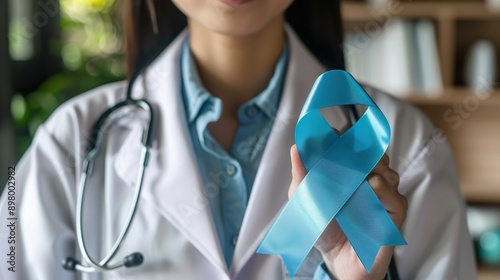 Portrait asian female doctor with stethoscope in uniform holding prostate cancer awareness campaing blue ribbon. photo