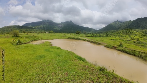 Scenic View of Sahyadri Hills with Pond, Lush Green Meadow, and Cloudy Sky during Monsoon Season