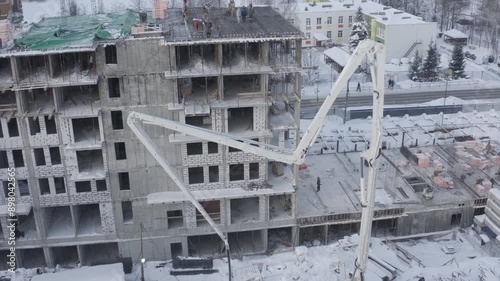 A drone view of the construction of a residential building using a concrete pump. Workers are building a house on a sunny winter day.