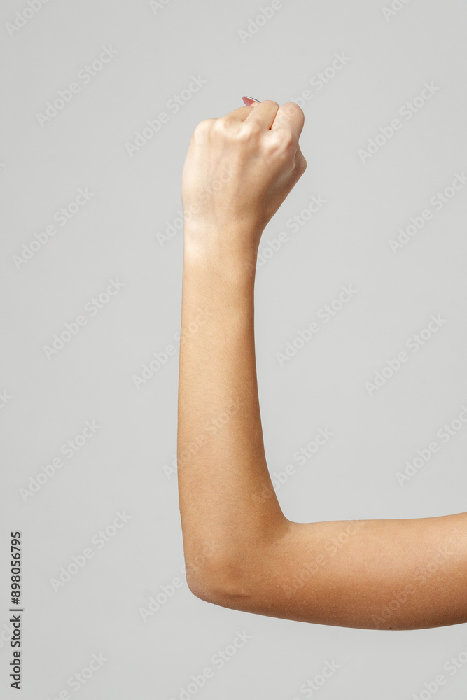 Close Up of Woman's Arm With Fist Raised in Front of a Grey Background Close Up of Woman's Arm With Fist Raised in Front of a Grey Background
