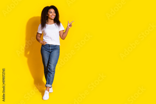 Full body portrait of nice young woman point finger empty space wear t-shirt isolated on yellow color background © deagreez