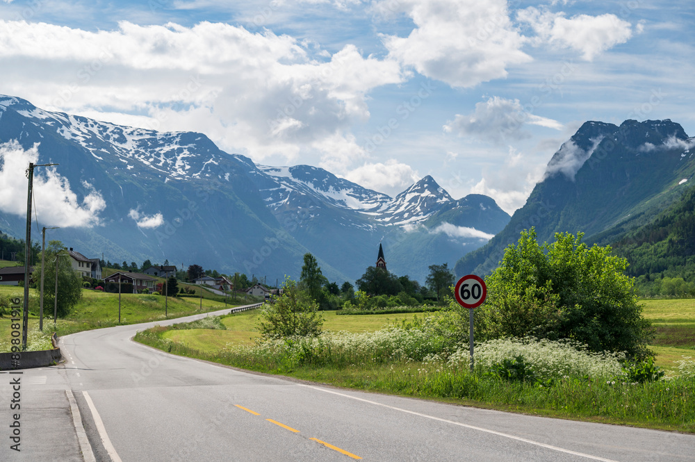 A quiet, rural road, through the beautiful Norwegian town of Olden, located deep in the Fjords of western Norway. A typical red Norwegian church can be seen in the distance A quiet, rural road, through the beautiful Norwegian town of Olden, located deep in the Fjords of western Norway. A typical red Norwegian church can be seen in the distance