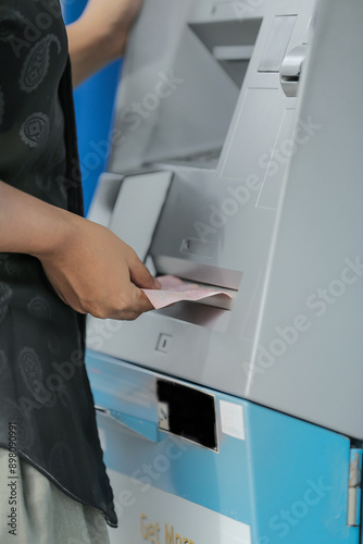 young woman withdrawing money with credit card from ATM machine typing pin code 