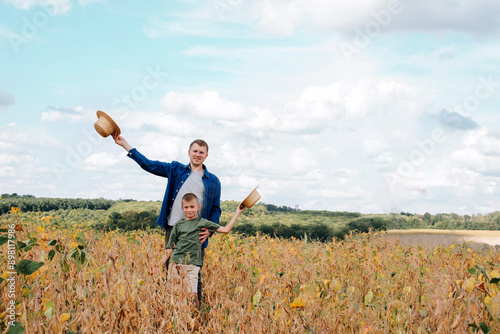 Agronomist, father and son together in agriculture field with soybeans. The man shows the boy ripe soy. Quality control of crops. Front view