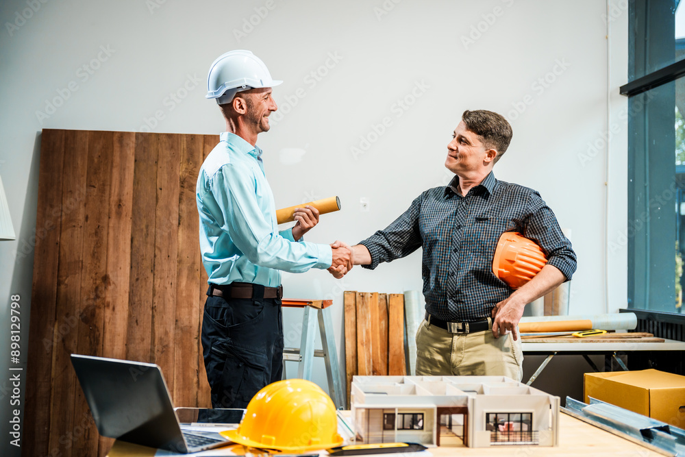 A Caucasian male engineer and an Italian male building contractor are planning and talking at a desk, reviewing house plans and a model of a house with wooden textures for renovation. A Caucasian male engineer and an Italian male building contractor are planning and talking at a desk, reviewing house plans and a model of a house with wooden textures for renovation.