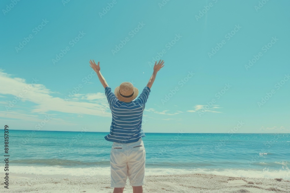 Young teenager with her arms raised in joy, standing on the beach facing an ocean view under clear blue skies. Young teenager with her arms raised in joy, standing on the beach facing an ocean view under clear blue skies.