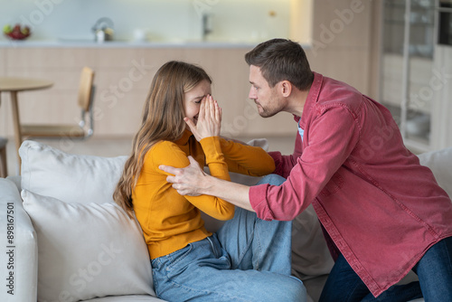 Tyrant husband shouting and shaking crying wife, arguing and grabbing her hands on sofa. Family quarrel, domestic violence and impossibility of escaping toxic relationships. Destructive power of abuse photo