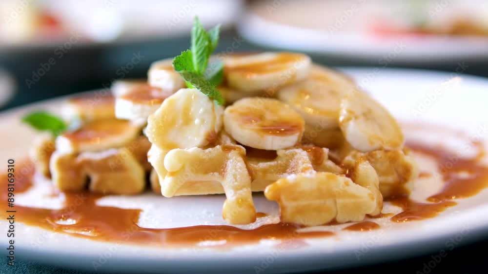 Waffles with banana and caramel white shirt pouring sweet syrup over the banana bread waffle on the table. Waffles with banana and caramel white shirt pouring sweet syrup over the banana bread waffle on the table.