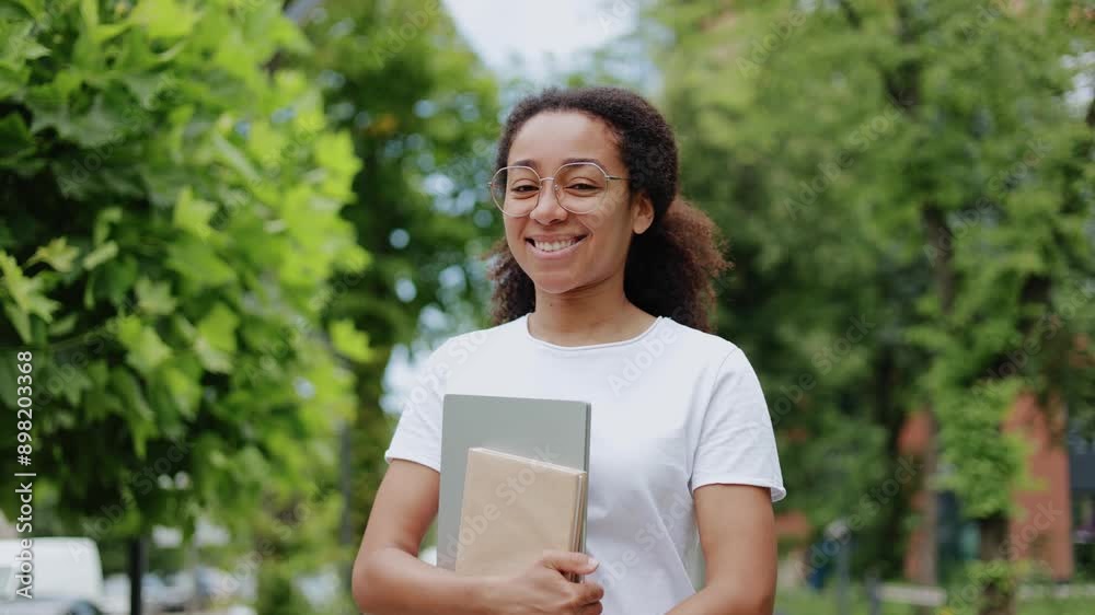 Portrait of smiling african american female with wireless laptop looking in camera while strolling outside. Pretty woman with glasses dressed in casual white enjoying good weather on street. Portrait of smiling african american female with wireless laptop looking in camera while strolling outside. Pretty woman with glasses dressed in casual white enjoying good weather on street.