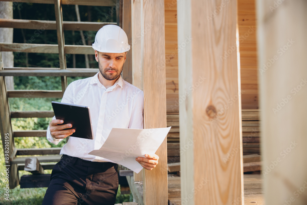 Man builder. Foreman studies blueprints with tablet. Contractor for construction company. Architect in unfinished building. Builder in house under construction. Man engineer from construction team Man builder. Foreman studies blueprints with tablet. Contractor for construction company. Architect in unfinished building. Builder in house under construction. Man engineer from construction team