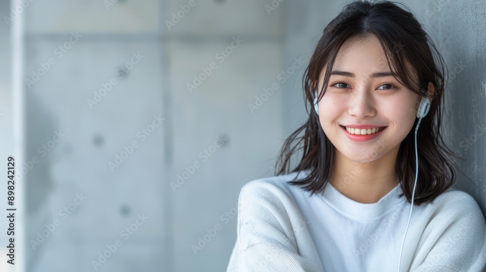 A woman in headphones, leaned against a wall, hands on hips, smiling at the camera A woman in headphones, leaned against a wall, hands on hips, smiling at the camera