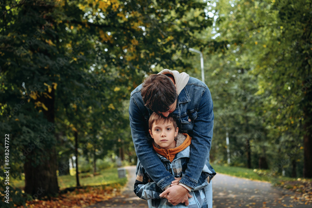 Caucasian man hugging his son in autumn park supporting sad boy