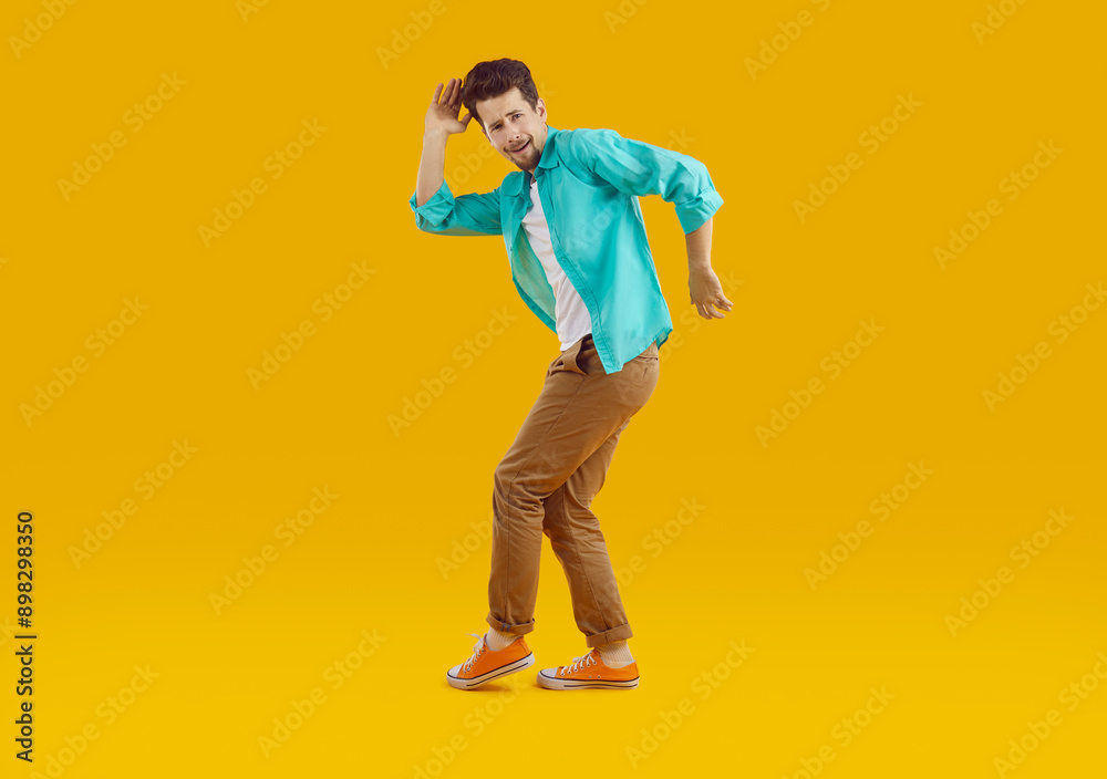 Full length portrait of brunet young bearded crazy cheerful man in turquoise shirt and brown pants funny dancing on yellow background. Disco, dance, banner for advertisement and marketing concept. Full length portrait of brunet young bearded crazy cheerful man in turquoise shirt and brown pants funny dancing on yellow background. Disco, dance, banner for advertisement and marketing concept.