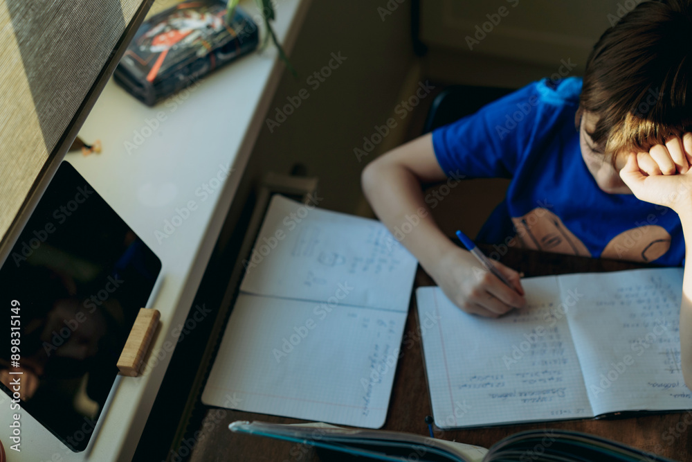stressed tired boy doing homework at home at the desk by the window. stressed tired boy doing homework at home at the desk by the window.