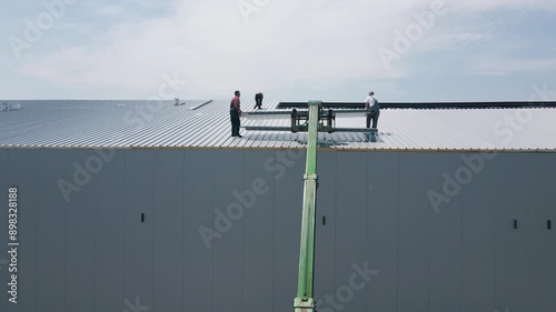 Metal building construction, workers lifting steel material on a factory roof during assembling.
