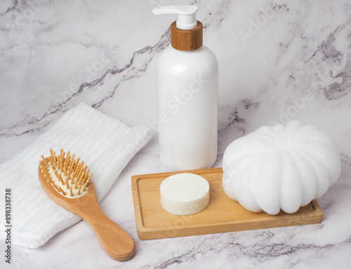 Set of body care products contained of white dispenser bottle, soap, wood hair brush, white loofah on marble background
