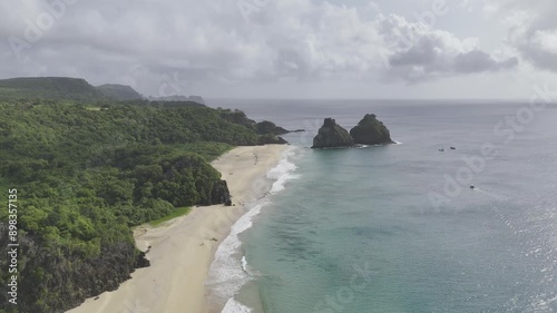 Drone lowers down to water from high over Praia do Boldró facing Praias do Americano, do Bode, da Cacimba do Padre and Morro Dois Irmãos on cloudy afternoon in Fernando de Noronha, Pernambuco photo