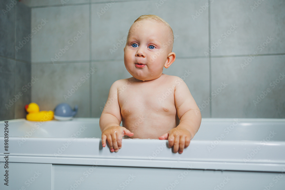 Baby boy bathes at home in a white bathtub with water. Baby smiling and happy splashing in the water at home. Baby boy bathes at home in a white bathtub with water. Baby smiling and happy splashing in the water at home.