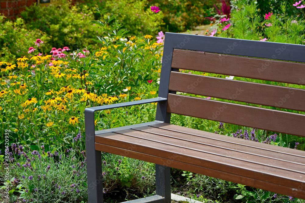 drewniana ławka ogrodowa w ogrodzie z kolorowymi kwiatami, wooden garden bench in the garden with colorful flowers, garden seating area
