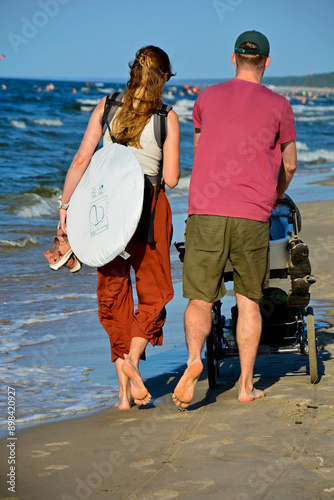 para młodych ludzi idąca plażą z wózkiem dzieciecym, couple of young people walking on the beach with a baby stroller, he and she on the beach with a stroller,Family walking along the beach front.

