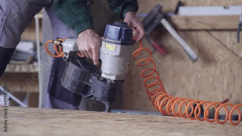 Woodworker uses pneumatic nail gun to hammer frame of wood hose building construction at workshop