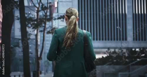 Successful Businesswoman in a Green Suit Walks Through a Modern City Street, Using a Digital Tablet. Professional lifestyle, Urban Lifestyle, and Digital Technology. photo