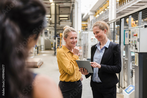 Happy businesswoman holding tablet PC and discussing with colleague at production floor