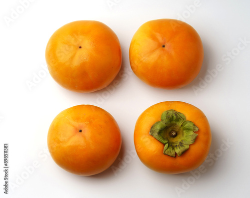 Close-up and top angle view of four ripe persimmons with turned one on white floor, South Korea 