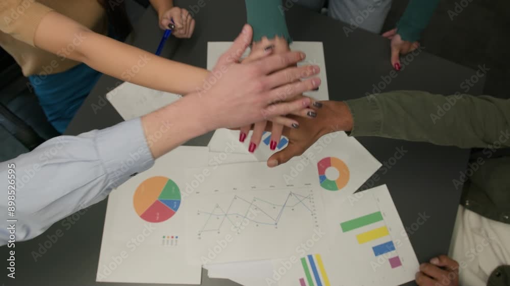 Top view paperwork on table hands stacking in pile diverse business team men women coworkers girls guys put arms together unity gesture union support motivation teamwork partnership win celebration