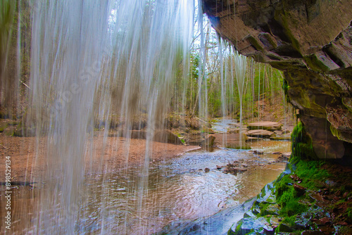 Fototapeta Naklejka Na Ścianę i Meble -  Landscape of a small waterfall viewed from behind as it cascades into Lost Creek in a peaceful forest on an early Spring day near Cornucopia, Wisconsin.