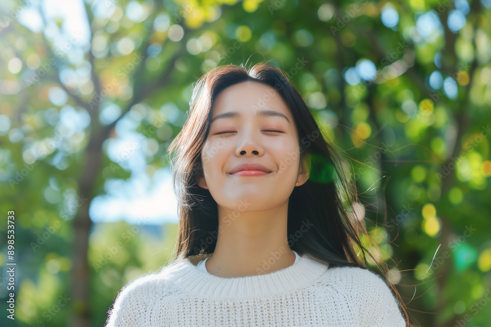 happy young asian woman in white sweater smiling with eyes closed outdoors, green trees background. Happy asian girl enjoying nature and taking deep breaths happy young asian woman in white sweater smiling with eyes closed outdoors, green trees background. Happy asian girl enjoying nature and taking deep breaths