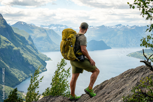 male backpacking hiker with yellow backpack climbing Romsdalseggen trail in Andalsnes Norway in summer with rocky mountains in the background photo